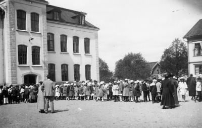 Ett antal personer på skolgård.
Nyckelord: Skolavslutning