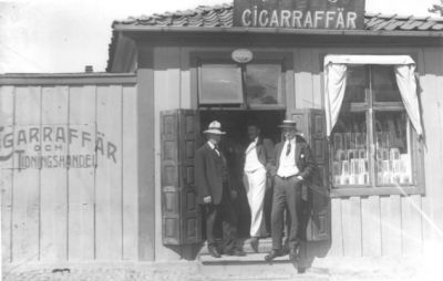 3 män stående på trappa till affär.
Nyckelord: Tobak