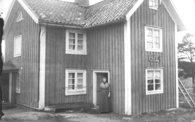 Kvinna i dörröppning till byggnad.
Nyckelord: Byggnad