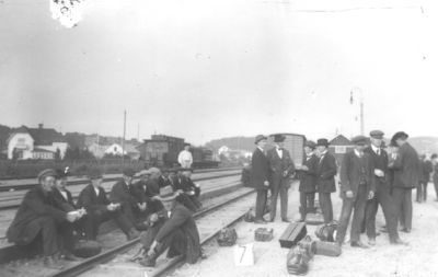 Ett antal stående och sittande män vid järnväg.
Nyckelord: Räls Perrong Unikabox