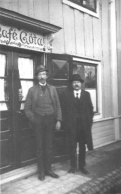 2 män stående framför café.
Nyckelord: Café