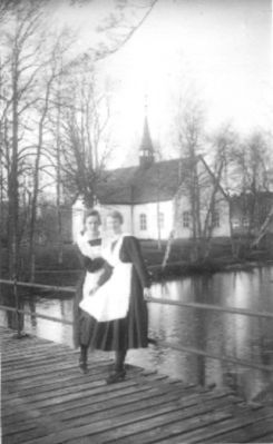 2 kvinnor på bro framför kyrka.
