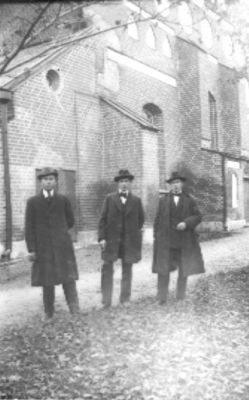 3 män stående framför kyrka.
