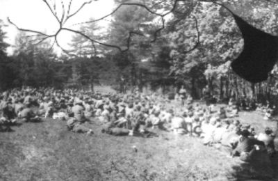 Ett antal personer sittande i skogsbacke.
Nyckelord: Skogsbacke Folksamling