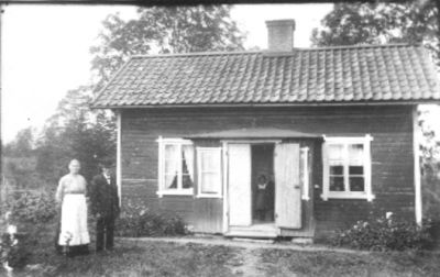 Man och kvinna stående framför byggnad och flicka stående i dörröppning.
