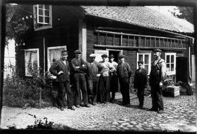 8 män stående framför byggnad.
Nyckelord: Kullersten