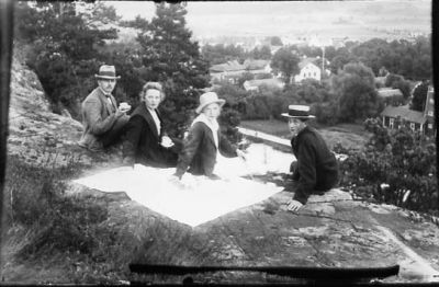 2 män och 2 kvinnor sittande på filt på berg med bebyggelse i bakgrunden.
Nyckelord: Utsikt