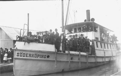 Ett antal personer stående på båt och på kaj.
