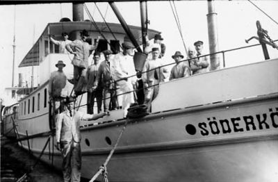 Ett antal män stående på och vid båt.
