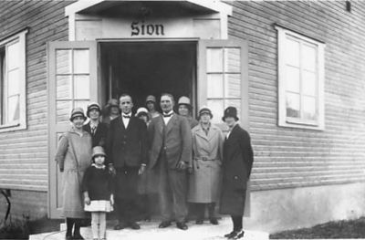 Ett antal personer stående i dörren till byggnad.
