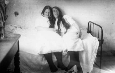 2 kvinnor sittande i säng.
Nyckelord: Säng