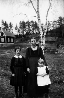 Kvinna och 2 barn stående på tomt.
