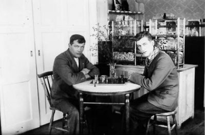 2 män sittande vid bord i café.
