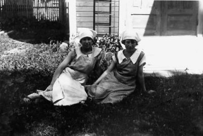 2 kvinnor sittande framför byggnad.
