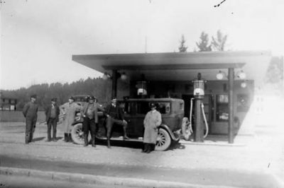 6 män stående framför bil på bensinstation.
Nyckelord: Bil