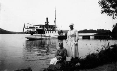 2 kvinnor framför båt vid brygga.
