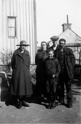 Familj stående framför husgavel.
