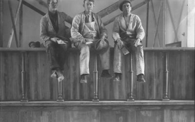 3 män sittande på räcke i sal.
