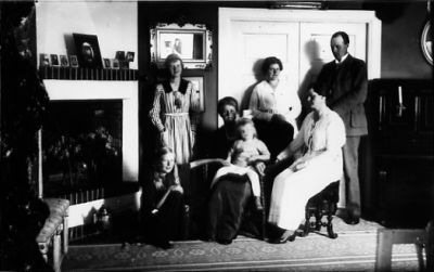 Familj sittande och stående i finrum.
