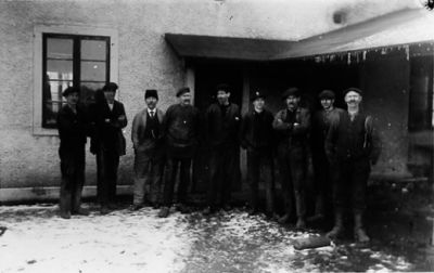 9 män stående framför byggnad.
