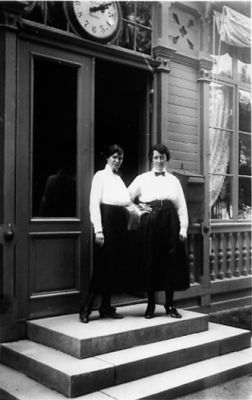 2 kvinnor stående på trappa till byggnad.
