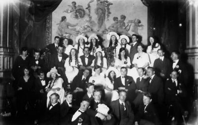 Ett antal högtidsklädda personer sittande och stående i lokal.
Nyckelord: Lokal Dräkt