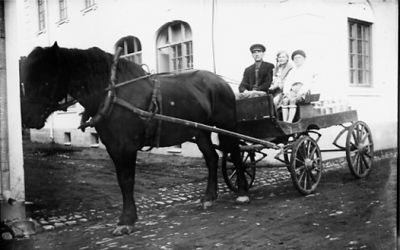 Man, pojke och flicka sittande på hästekipage.
Nyckelord: Häst Vagn Mjölkkrukor