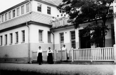 3 kvinnor stående framför byggnad.
Nyckelord: Staket Träd Acasia