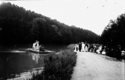 Ett antal personer stående på färja och på land.
Nyckelord: Färja