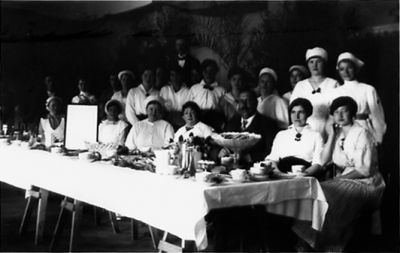 Ett antal personer sittande och stående vid långbord.
Nyckelord: Dräkt