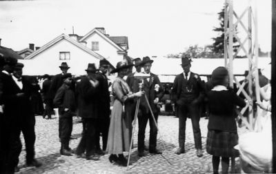 Ett antal personer stående på torg varav en kvinna med kamera.
Nyckelord: Kullersten