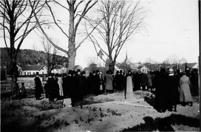 Ett antal personer på begravningsplats.
Nyckelord: Kyrka