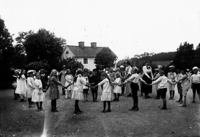 Kvinnor och barn dansande ringlekar.
