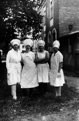 4 kvinnor stående på gård.
Nyckelord: Huvudbonad