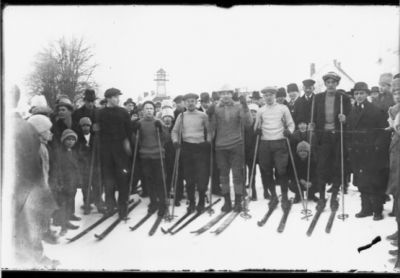 6 män stående på skidor bland ett antal barn och vuxna utan skidor.
Nyckelord: Skidor Stavar Snö