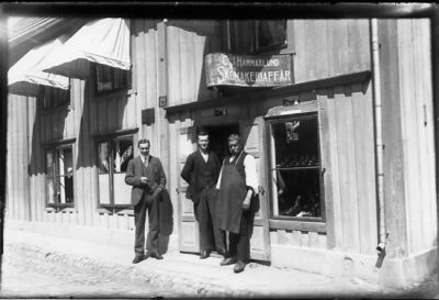 3 män stående i dörröppning.
Nyckelord: Affärsskylt