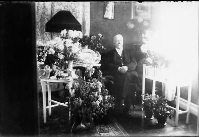 Man sittande i rum med blommor runt sig.
Nyckelord: Blommor