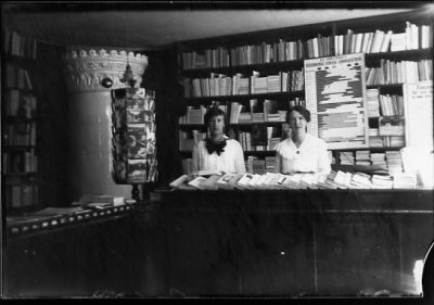 2 kvinnor stående bakom disken i bokhandel.
Nyckelord: Kakelugn Affärsinredning