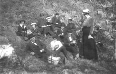 Ett antal personer liggande i en skogsbacke.
Nyckelord: Kaffekorg Dräkt Hatt