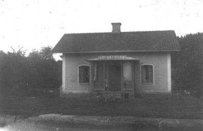 Flicka stående på verandan till byggnad.
Nyckelord: Skylt