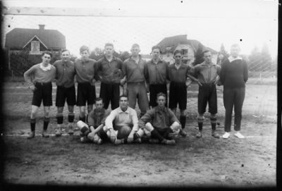 9 män stående och 3 sittande på fotbollsplan.
Nyckelord: Idrottsplats