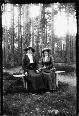 2 kvinnor sittande på bänk i skog.
Nyckelord: Bänk Skog Dräkt