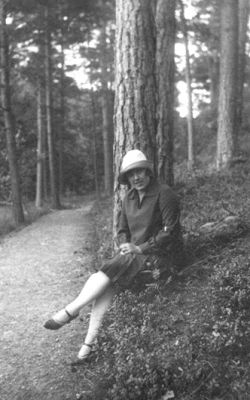 Kvinna sittande vid stig.
Nyckelord: Skogsbacke Stig Skog