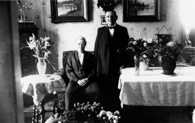 Man stående och kvinna sittande i rum med blommor.
Nyckelord: Blommor Tavla
