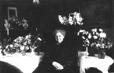 Kvinna sittande i rum med blommor.
Nyckelord: Blommor