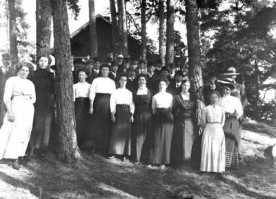 En grupp män och kvinnor i en skogsbacke framför en byggnad
