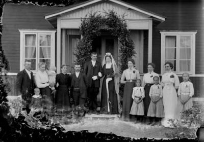 Brudpar och bröllopsgäster stående framför byggnad
Nyckelord: Äreport Dräkt