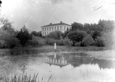 Kvinna vid vattendrag intill herrgård

