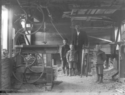 Man och 3 pojkar stående i verkstad
Nyckelord: såg virke