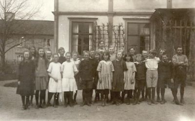 Skolklass med lärarinna framför byggnad
